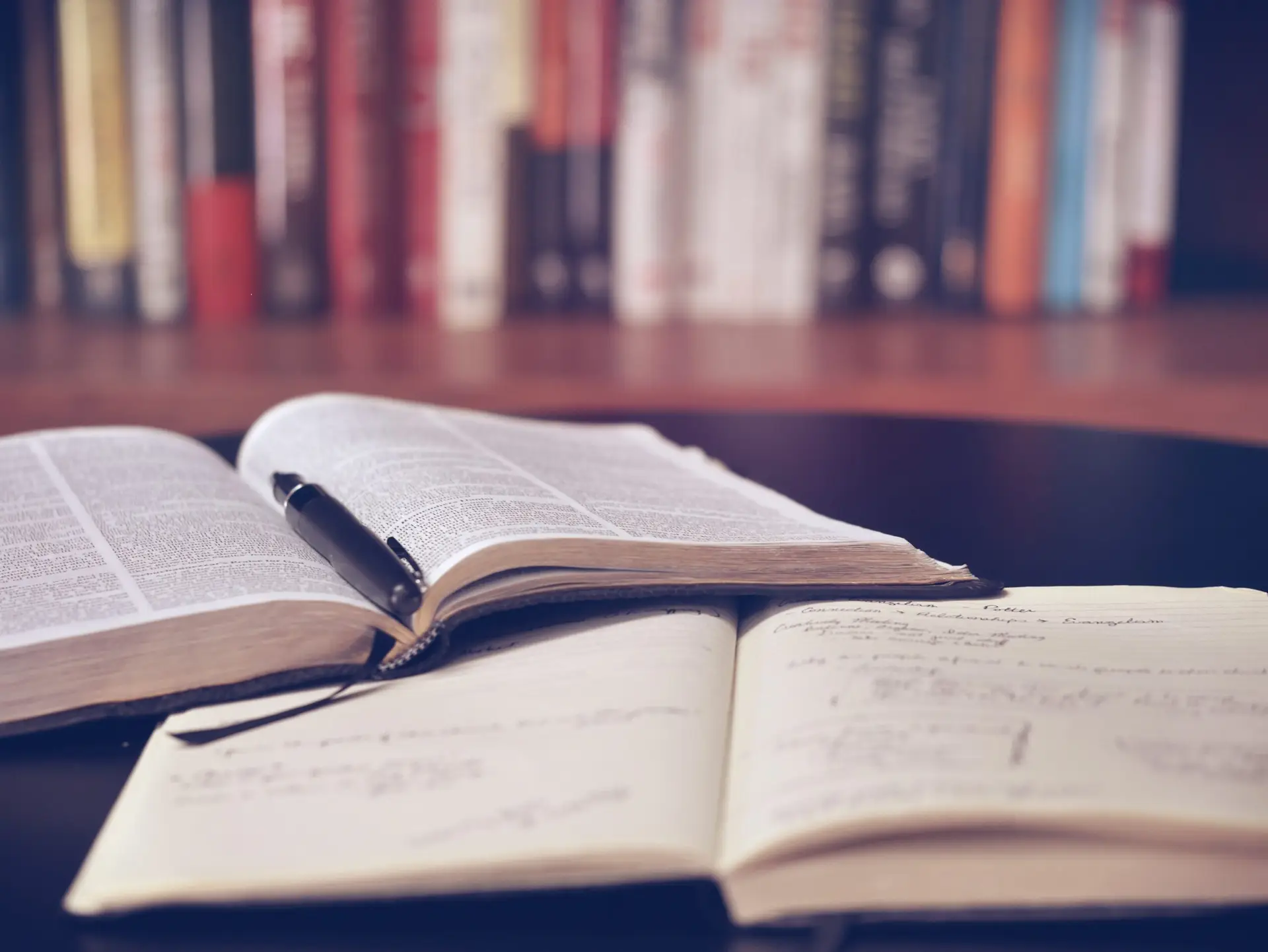 Open book and notepad laying on a table in a library