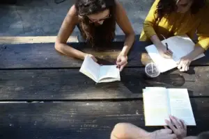 Three people engaged in active learning with books and notes on a wooden table.
