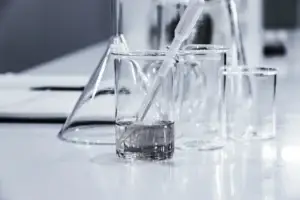 Laboratory glassware on a shiny surface with a pipette adding liquid to a beaker.