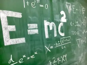 Chalkboard with physics equations, including Einstein's mass-energy equivalence formula.