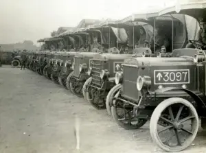 Historic photo of a row of early World War I military ambulances lined up with soldiers seated inside.