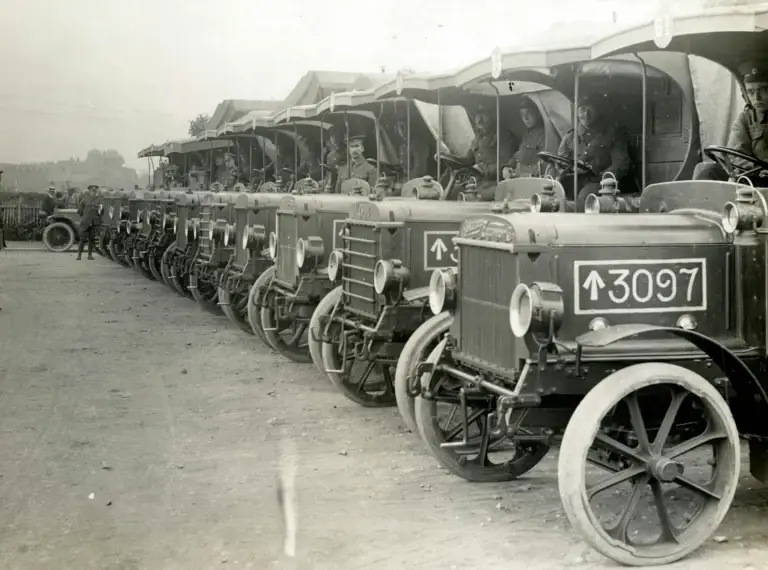 Historic photo of a row of early World War I military ambulances lined up with soldiers seated inside.