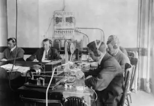 Black and white historical photo of individuals with early 20th-century radio equipment, possibly intercepting communications